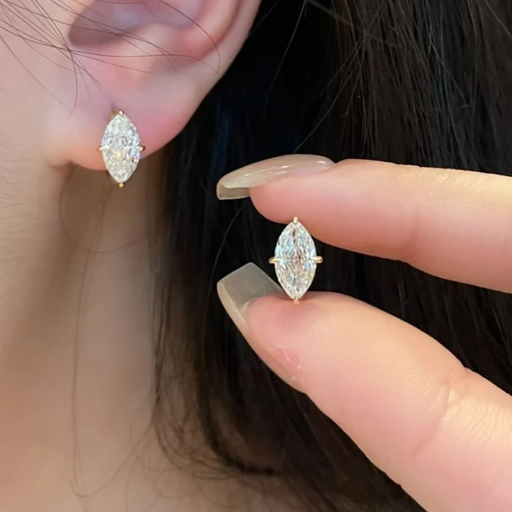 Marquise-cut lab-grown diamond stud earrings in yellow gold, one worn and one held between fingertips