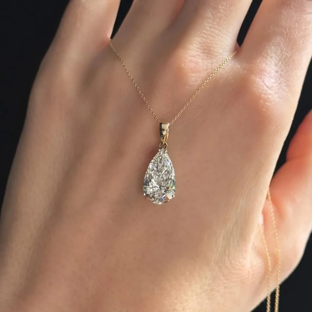 A pear-shaped lab-grown diamond solitaire pendant on a fine yellow gold chain draped over a hand