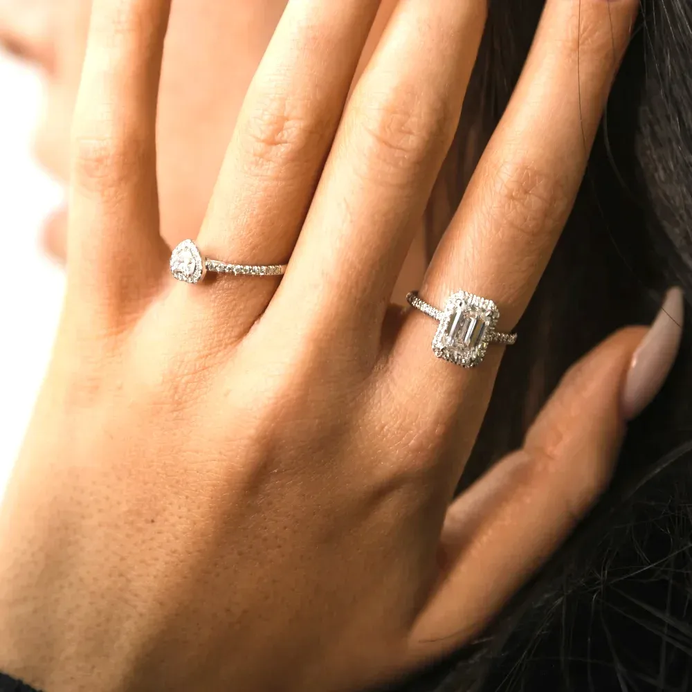 A hand wearing a round halo diamond ring and an emerald-cut lab-grown diamond ring