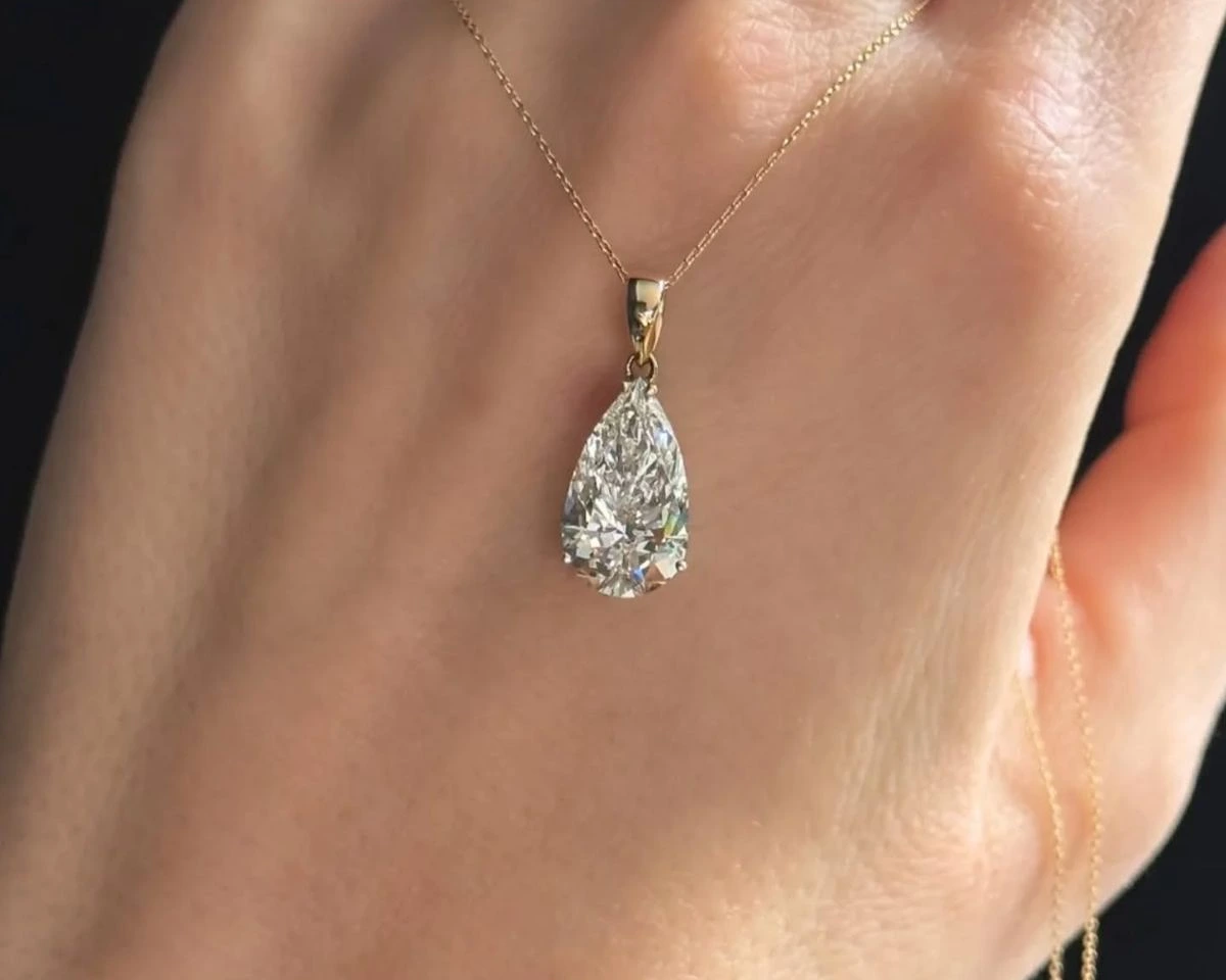 A pear-shaped lab-grown diamond solitaire pendant on a fine yellow gold chain draped over a hand