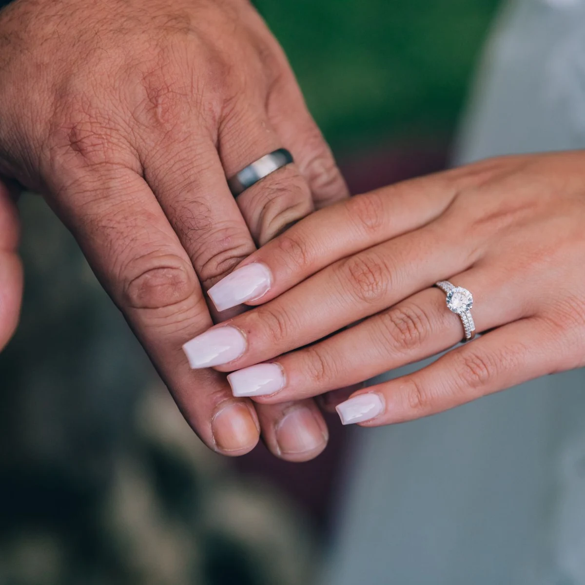 A couple’s hands resting together, his brushed wedding band beside her diamond engagement ring