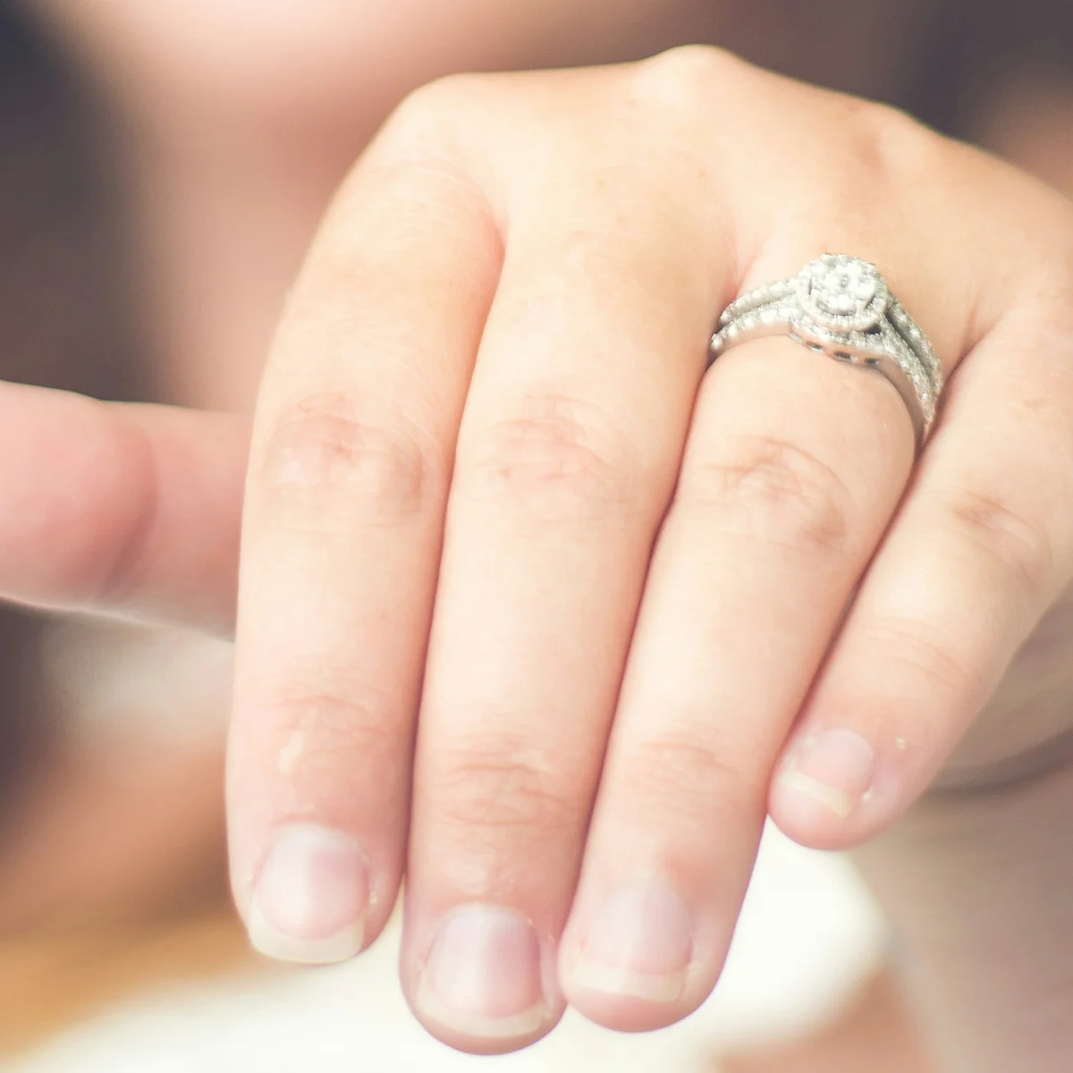 A hand held out to show a halo lab-grown diamond engagement ring with a pavé band