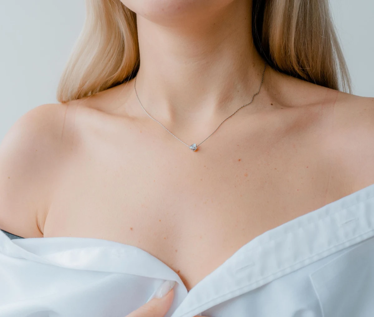 A woman in an off-the-shoulder white shirt wearing a lab-grown diamond solitaire pendant on a fine chain