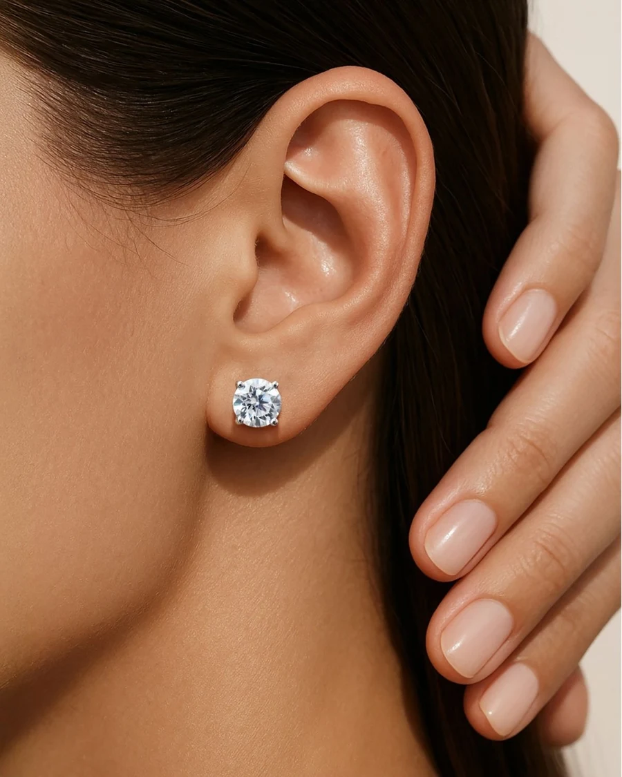 Close-up of a round lab-grown diamond stud earring on a woman’s ear, her hand resting by her hair