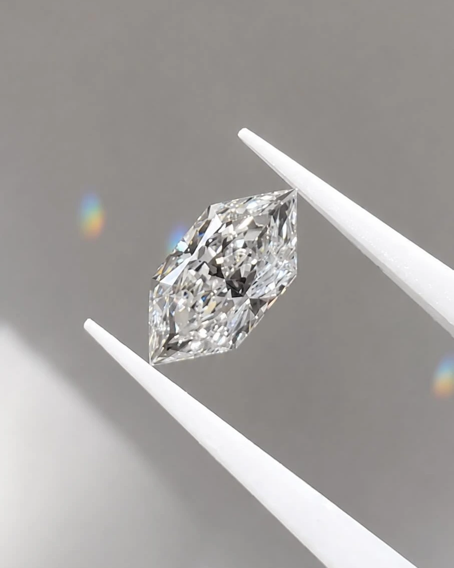 An elongated hexagon-cut lab-grown diamond held in white tweezers, casting rainbow light